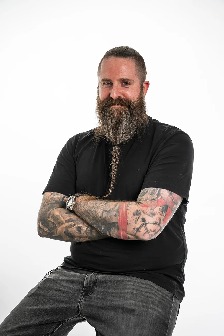 Tim Grubbert, stehend mit verschränkten Armen, tätowierte Unterarme, schwarzes Shirt
