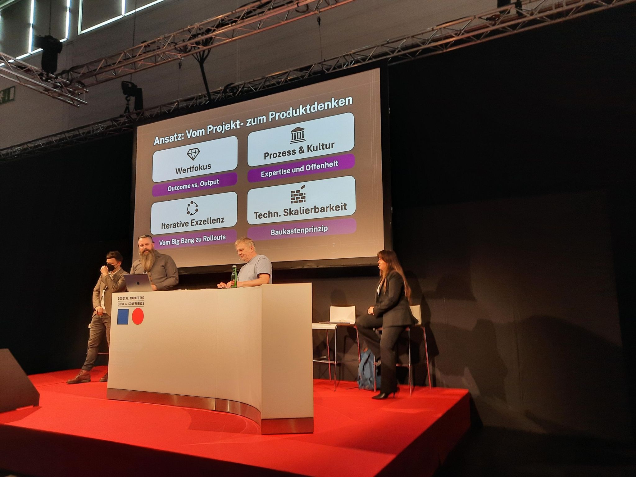 Tim Grubbert auf der DMEXCO-Bühne, roter Bühnenboden, Folie ‚Vom Projekt- zum Produktdenken‘